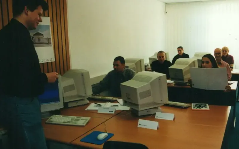 Der erste Schulungsraum von INCAS Training aus 1998 Ein Klassenzimmer mit sechs Personen, die mit Desktop-Computern arbeiten, während der Trainer, Stephan Otten, vorne steht und unterrichtet.